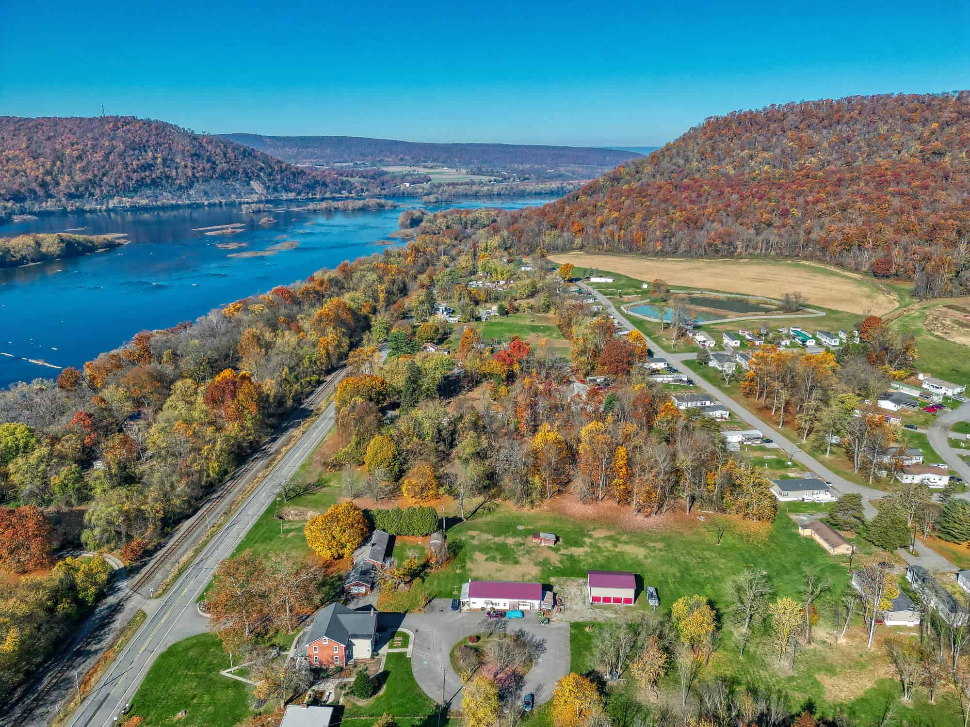 Drone view of two mountains and a river flowing through the center with farm houses in valley.