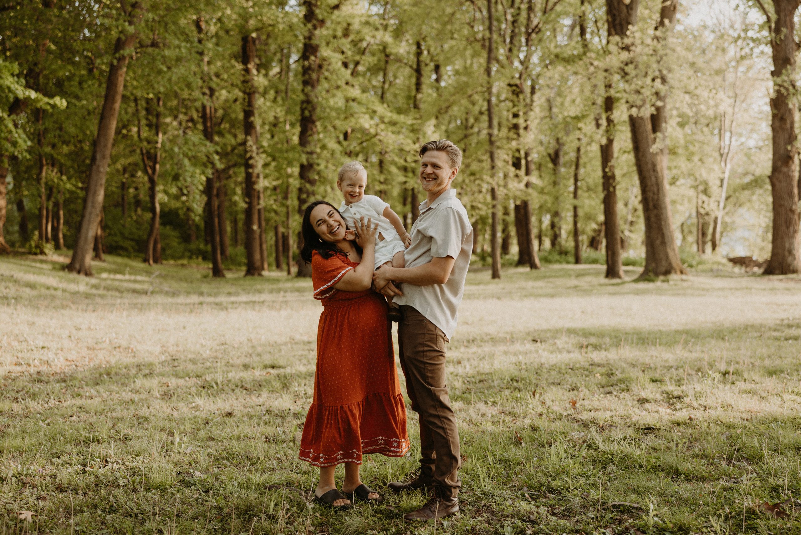 Young family standing in a field with pregnant mom and toddler son and father.